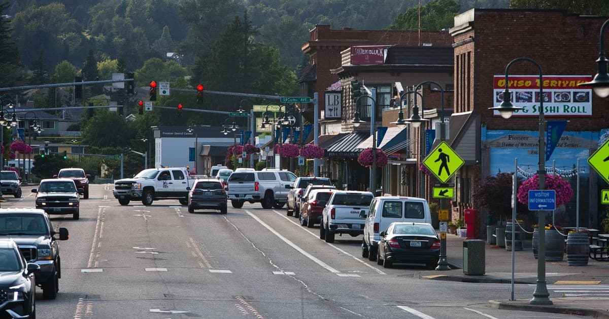 Lively urban street with cars, shops, and pedestrians during daytime.