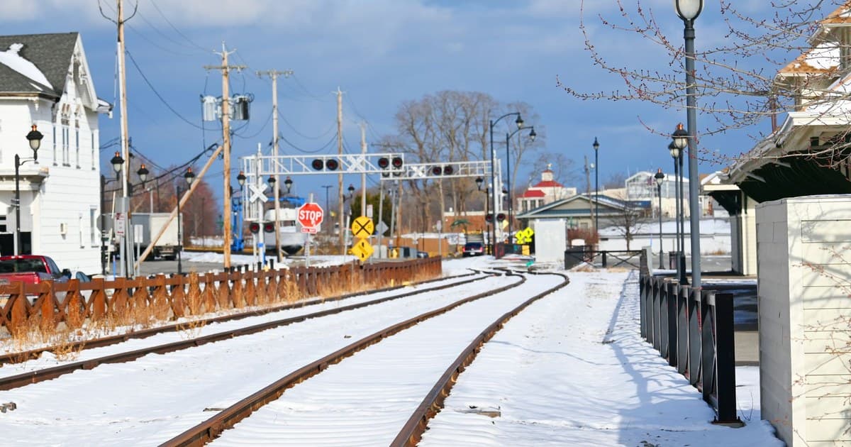 A scenic view of snow-covered train tracks in a small town setting during winter.